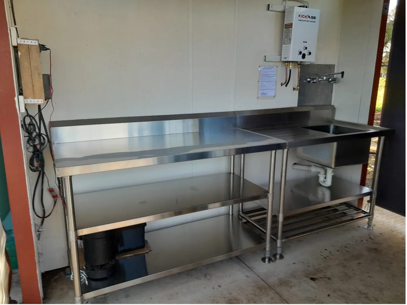 The new stainless steel kitchen benches and sink, with a gas hot water unit mounted on the wall above