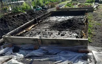 A wicking bed part-stripped, with soil pulled back and the liner exposed
