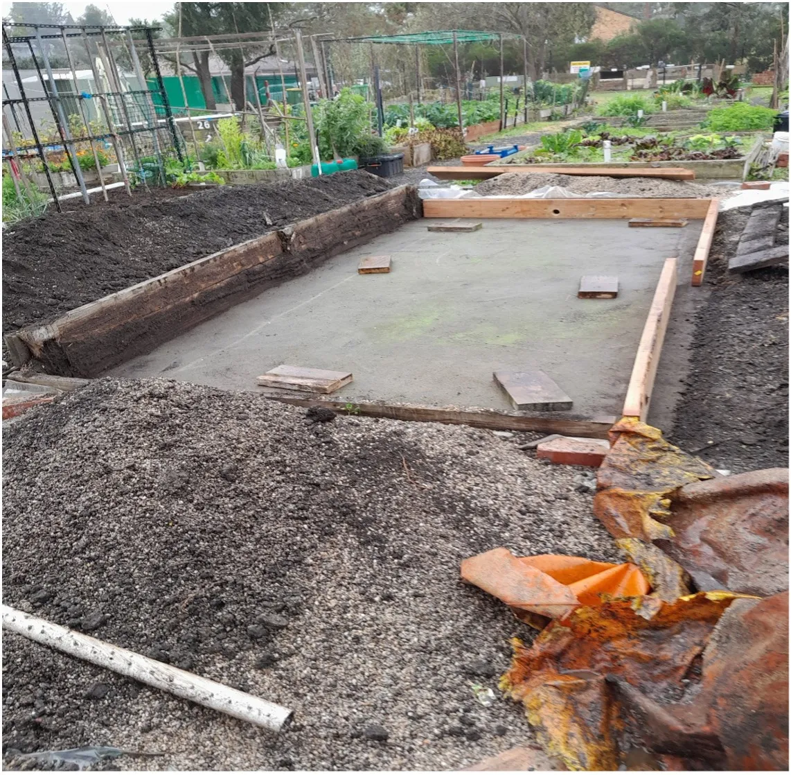The swept bowling-green base with new timber laid out around it, soil and gravel heaped to the sides