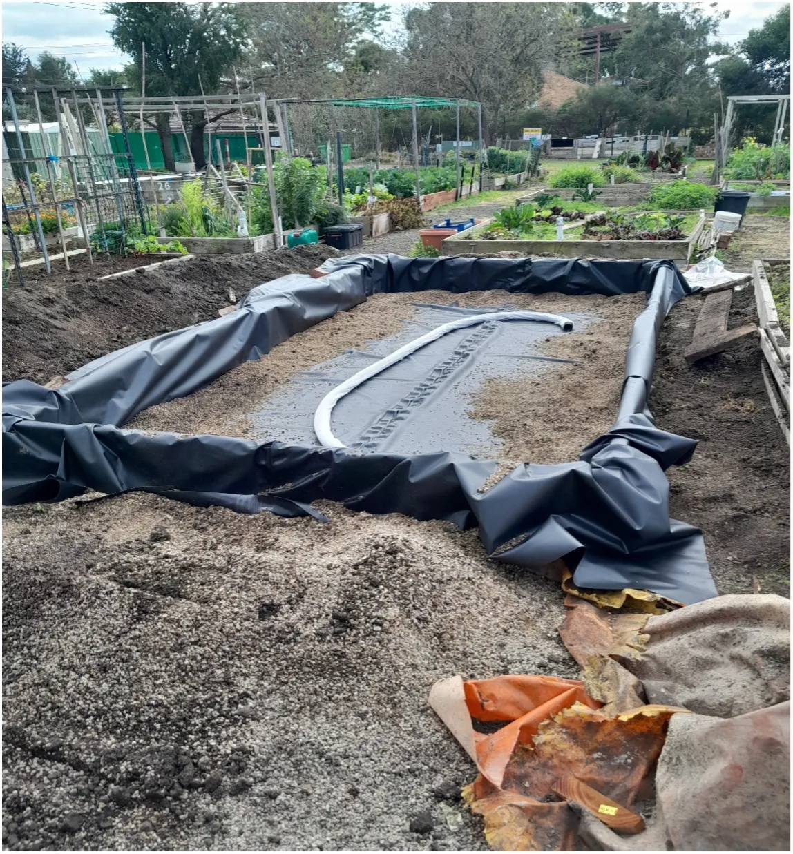 Black plastic liner in place with gravel weighting the edges and sock-covered Agi pipe rolled out along the base